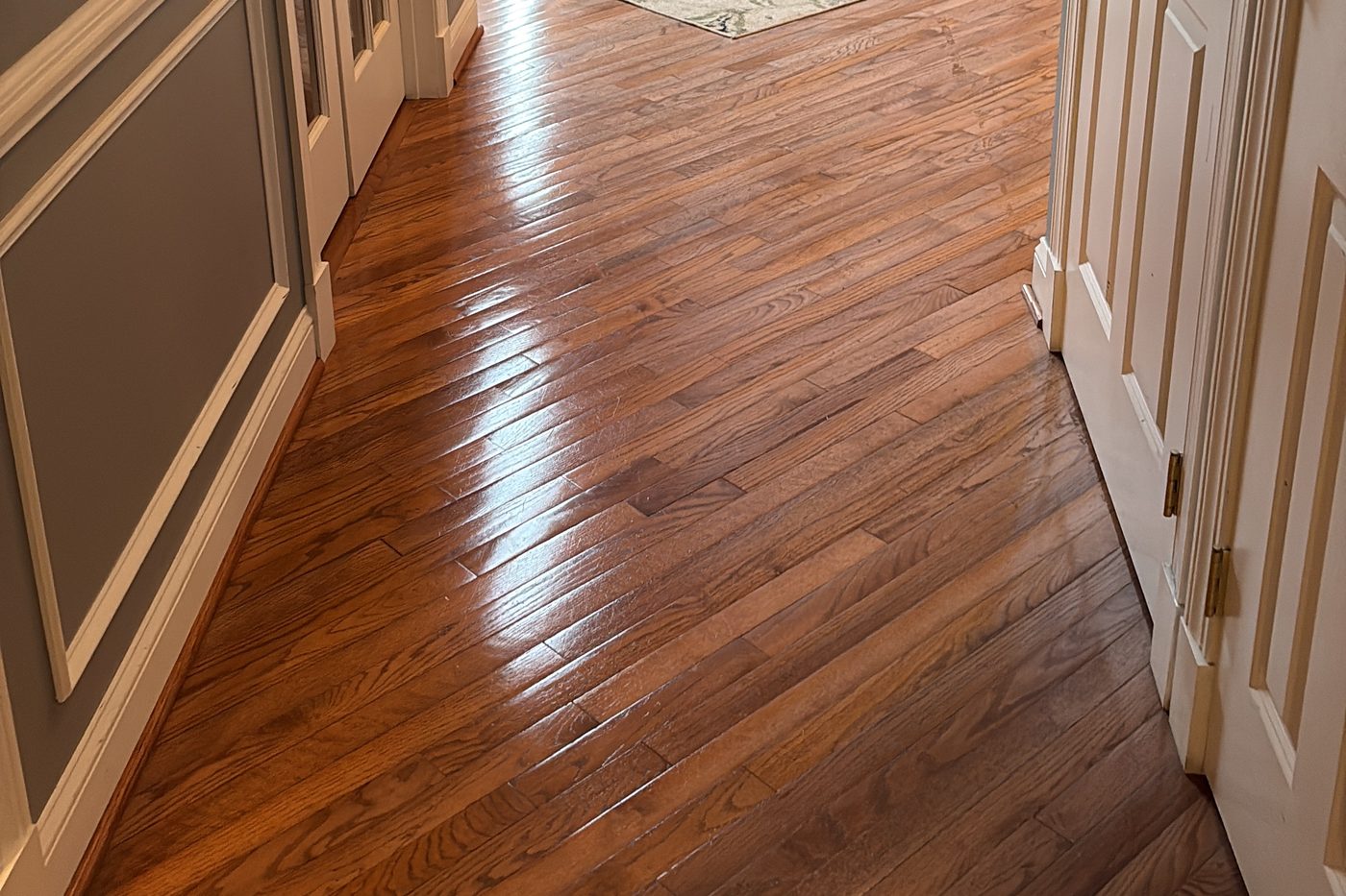 Polished hardwood hallway floor with white wainscoting and panelled doors after a cleaning visit